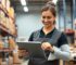 Quản lý bán hàng sử dụng tablet để theo dõi tồn kho real-time và quản lý hàng hóa trong cửa hàng bán lẻ, nền là kệ hàng được sắp xếp gọn gàng